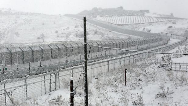 Ein schneebedeckter Grenzzaun mit Stacheldraht erstreckt sich durch eine hügelige Landschaft.