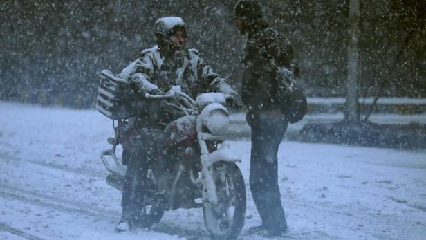 Ein Mann auf einem Motorrad spricht mit einer anderen Person im Schneefall.