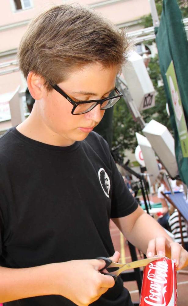 Ein Jugendlicher schneidet eine Coca-Cola-Dose mit einer Schere auf.