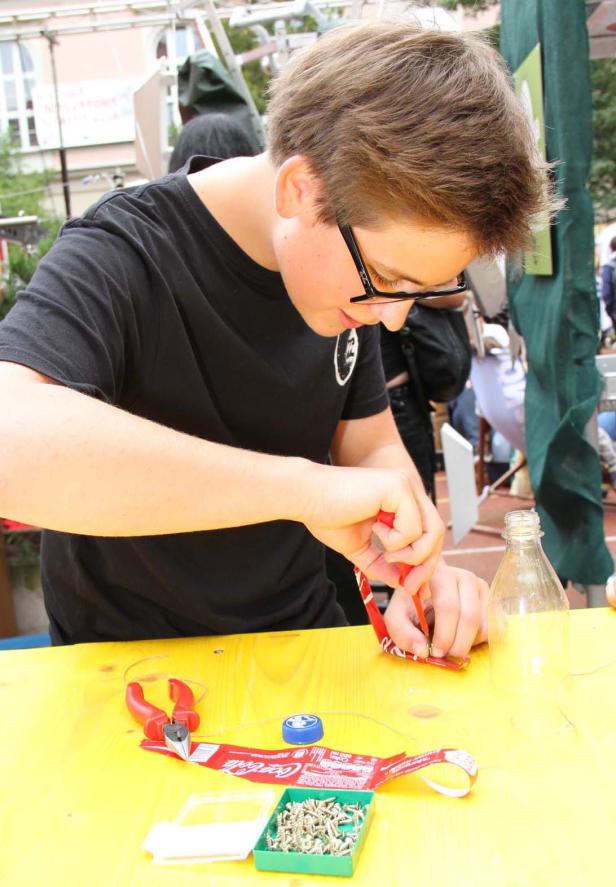 Ein Jugendlicher bastelt mit Werkzeug und einer Coca-Cola Dose an einem gelben Tisch.