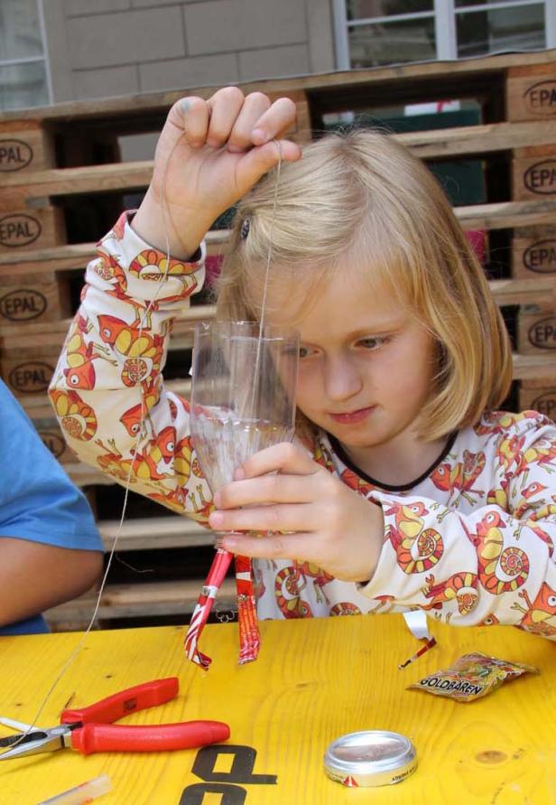 Ein Mädchen bastelt mit einer Plastikflasche und Süßigkeiten an einem Tisch.