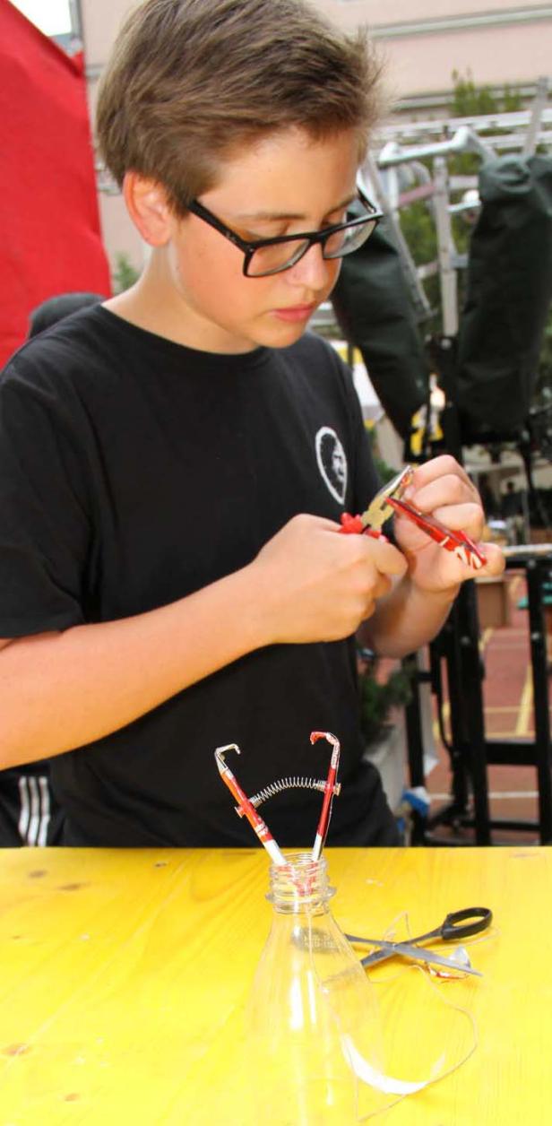 Ein Jugendlicher mit Brille bastelt an einem Werkstück mit Zange und Stiften.