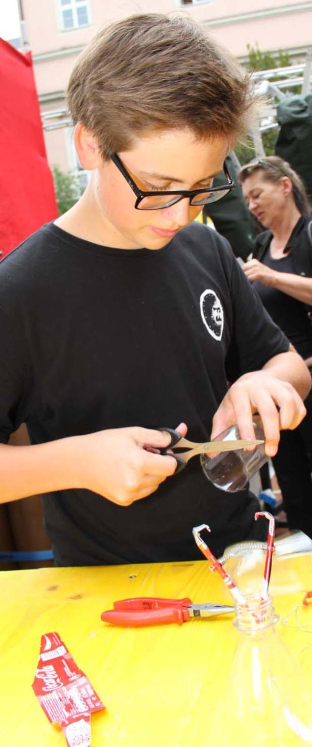 Ein Jugendlicher mit Brille schneidet eine Plastikflasche mit einer Schere.