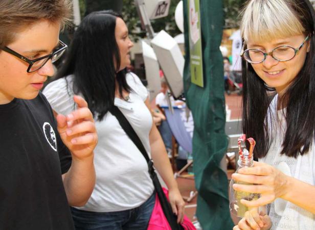 Eine junge Frau bastelt mit einer Plastikflasche, während ein Jugendlicher zusieht.
