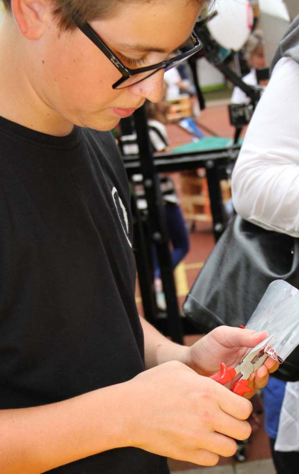 Ein Jugendlicher mit Brille benutzt eine Zange, um etwas zu bearbeiten.