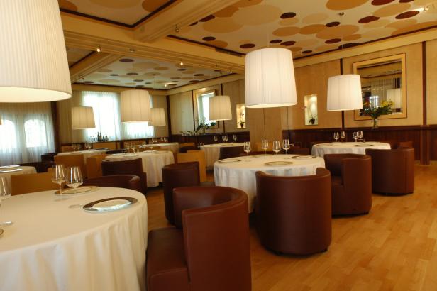 Ein elegant gedeckter Tisch in einem hellen Restaurant mit runden Tischen und braunen Sesseln.