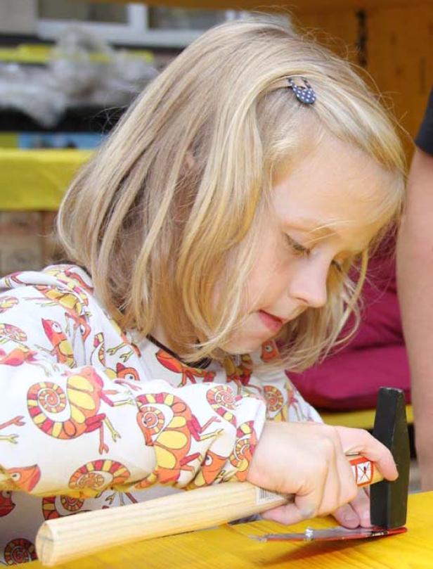 Ein blondes Mädchen hämmert auf einem gelben Tisch.