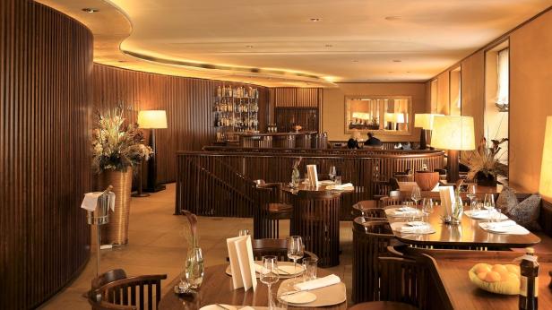 Innenansicht eines eleganten Restaurants mit gedeckten Tischen und einer Bar im Hintergrund.