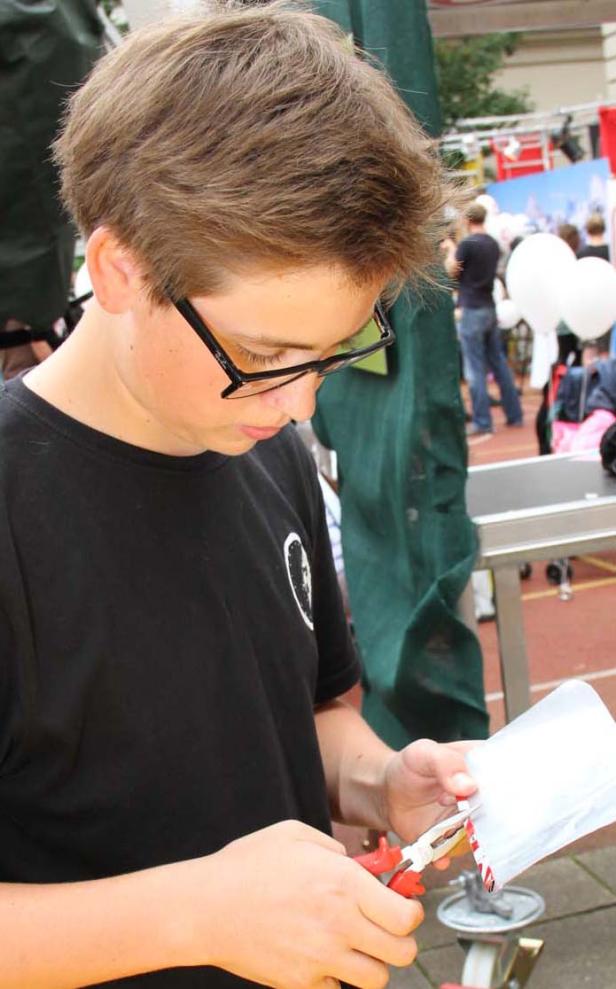 Ein Jugendlicher mit Brille schneidet mit einer Zange etwas aus einer weißen Tüte.