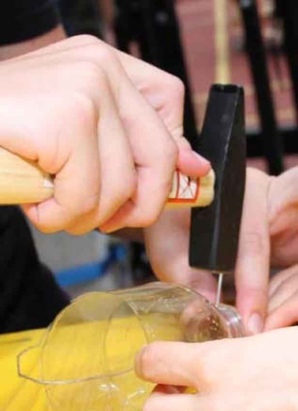 Eine Person hämmert einen Nagel in ein Stück Plastik, um einen Draht zu befestigen.
