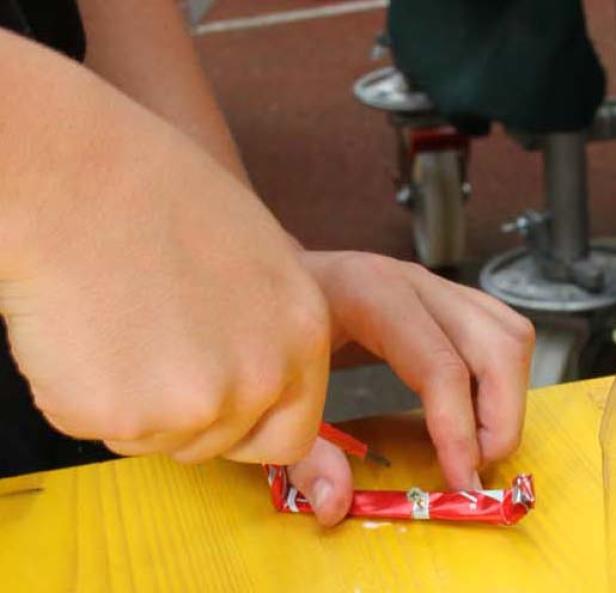 Eine Person bastelt mit einer roten Süßigkeitenverpackung auf einem gelben Tisch.