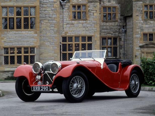 Ein roter Oldtimer-Sportwagen steht vor einem steinernen Gebäude.