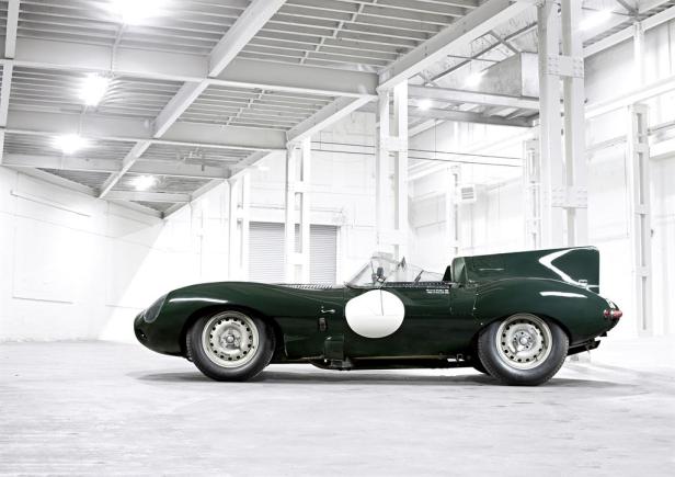 Ein grüner Jaguar D-Type Rennwagen steht in einem hellen, industriellen Raum.