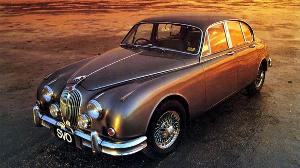 Ein klassischer Jaguar vor einem orangefarbenen Himmel.