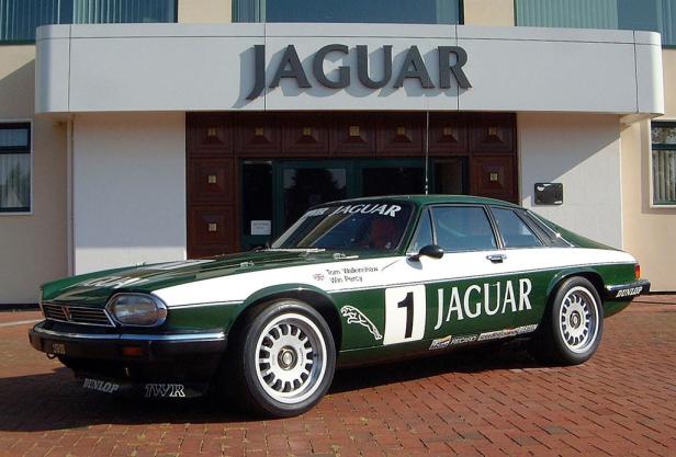 Ein grüner und weißer Jaguar XJS Rennwagen vor einem Jaguar-Gebäude.