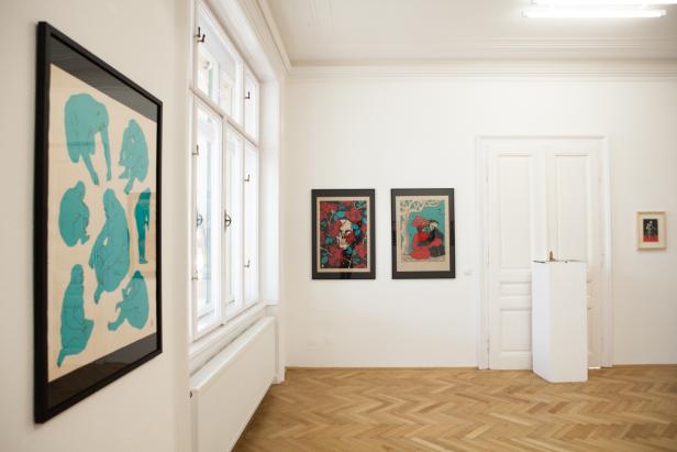 In einer Kunstgalerie hängen mehrere gerahmte Bilder an weißen Wänden.