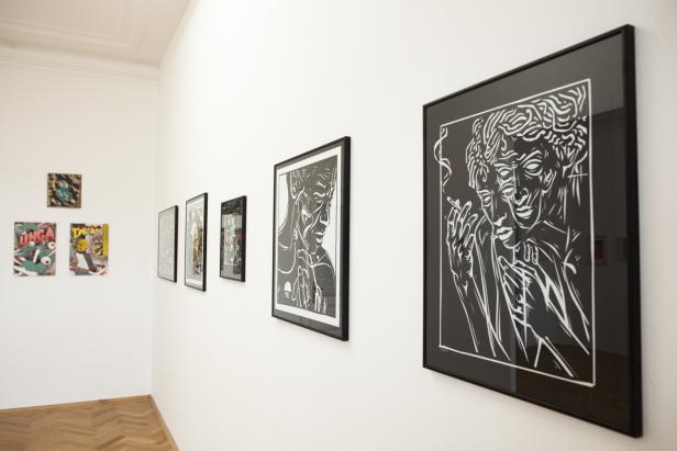 In einer Kunstgalerie hängen mehrere gerahmte Bilder an einer weißen Wand.