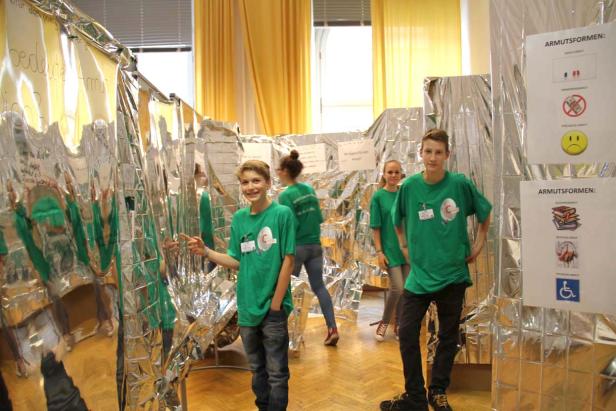 Eine Gruppe Jugendlicher steht vor einer Installation zum Thema Armut.