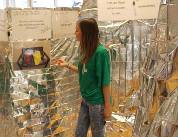 Ein junges Mädchen steht vor einer Installation mit silberner Folie und Botschaften zum Thema Armut.