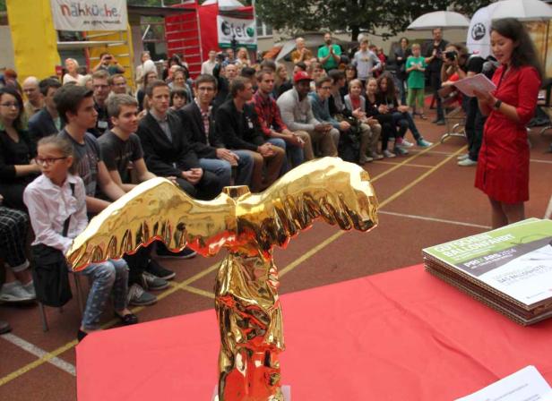 Eine goldene Statue steht vor einer Menschenmenge bei einer Preisverleihung.