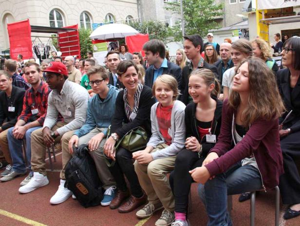 Eine Gruppe von Menschen sitzt draußen auf Stühlen und schaut zu.