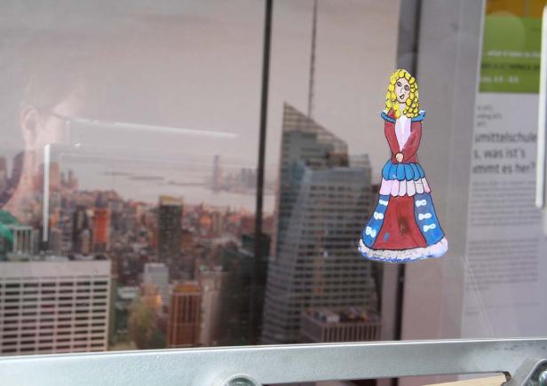Eine Kinderzeichnung einer Prinzessin klebt an einem Fenster mit Blick auf eine Stadt.