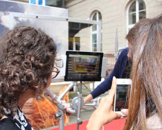 Zwei Frauen betrachten einen Bildschirm und machen Fotos mit ihren Smartphones.