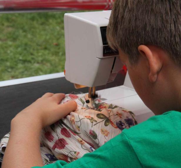 Eine Person näht ein Kleidungsstück mit Blumenmuster an einer Nähmaschine.