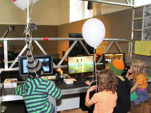 Kinder spielen an Computern, dekoriert mit Luftballons, auf einer Veranstaltung.