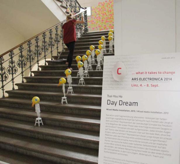 Eine Frau geht eine Treppe hinauf, auf der Installationen mit gelben Vogelköpfen stehen.