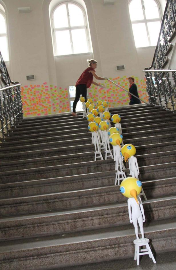 Eine Frau hantiert mit einer Stange auf einer Treppe, auf der Vogel-Skulpturen stehen.