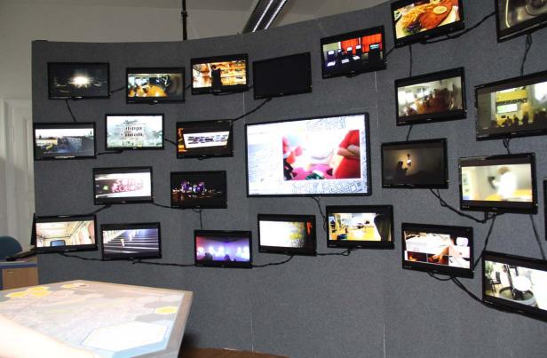 Eine Wand ist mit mehreren kleinen Bildschirmen bestückt, die verschiedene Szenen zeigen.