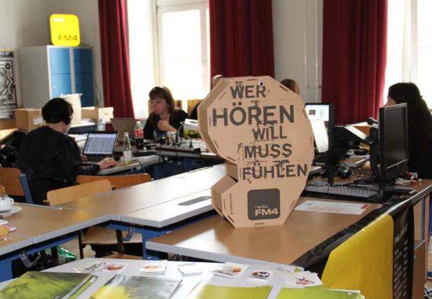 Ein Aufsteller von Radio FM4 mit dem Slogan „Wer hören will muss fühlen“ in einem Büro.