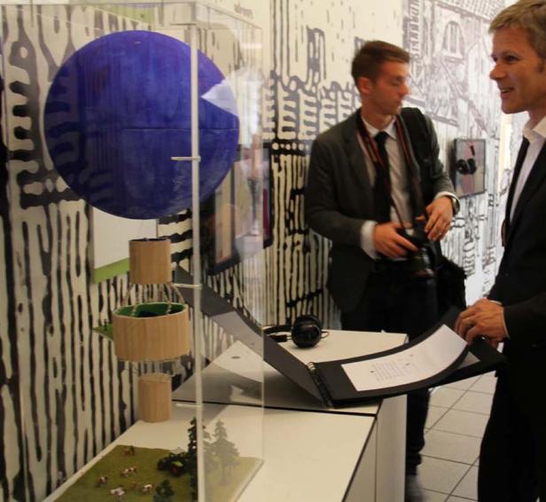 Zwei Männer betrachten eine Kunstinstallation mit einer blauen Kugel und einem Miniatur-Bauernhof.