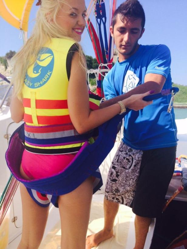 Eine Frau wird für das Parasailing vorbereitet, während ein Mann ihr hilft, den Gurt anzulegen.