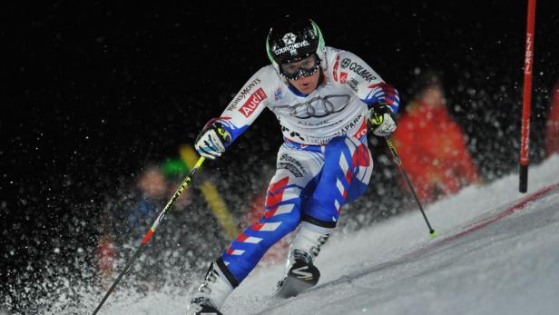 Ein Skirennfahrer in blau-weißer Kleidung fährt einen Hang hinunter.