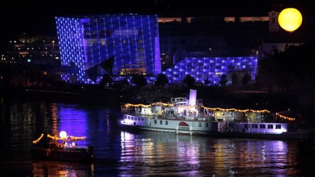 Ein beleuchtetes Gebäude und zwei Schiffe auf einem Fluss bei Nacht.