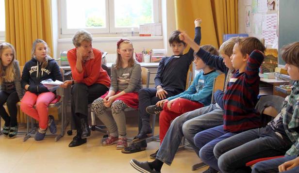 Eine Lehrerin sitzt mit einer Gruppe von Schülern im Klassenzimmer.