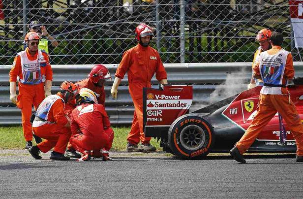 Rennstreckenpersonal umgibt einen beschädigten Ferrari-Rennwagen.