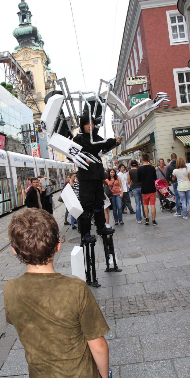 Ein Straßenkünstler in einer Roboter-ähnlichen Stelzenkonstruktion tritt in der Linzer Innenstadt auf.