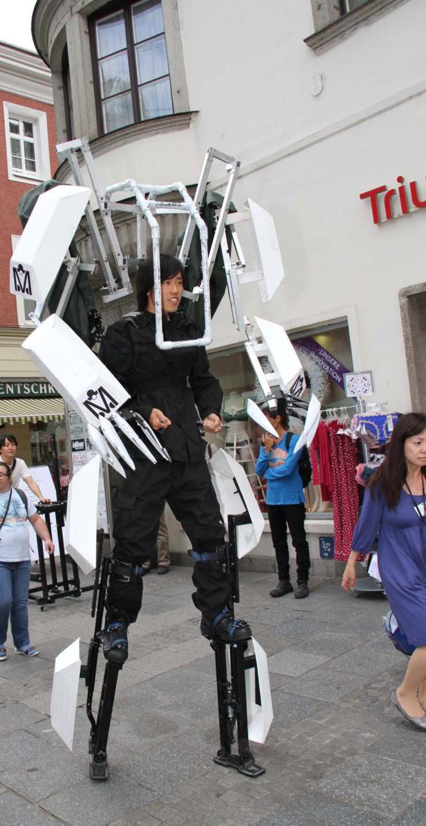 Ein Mann in einem Roboter-Kostüm steht auf Stelzen in einer belebten Straße.