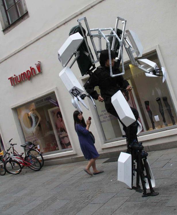 Ein Mann in einem Roboter-Kostüm steht vor einem Triumph-Geschäft.