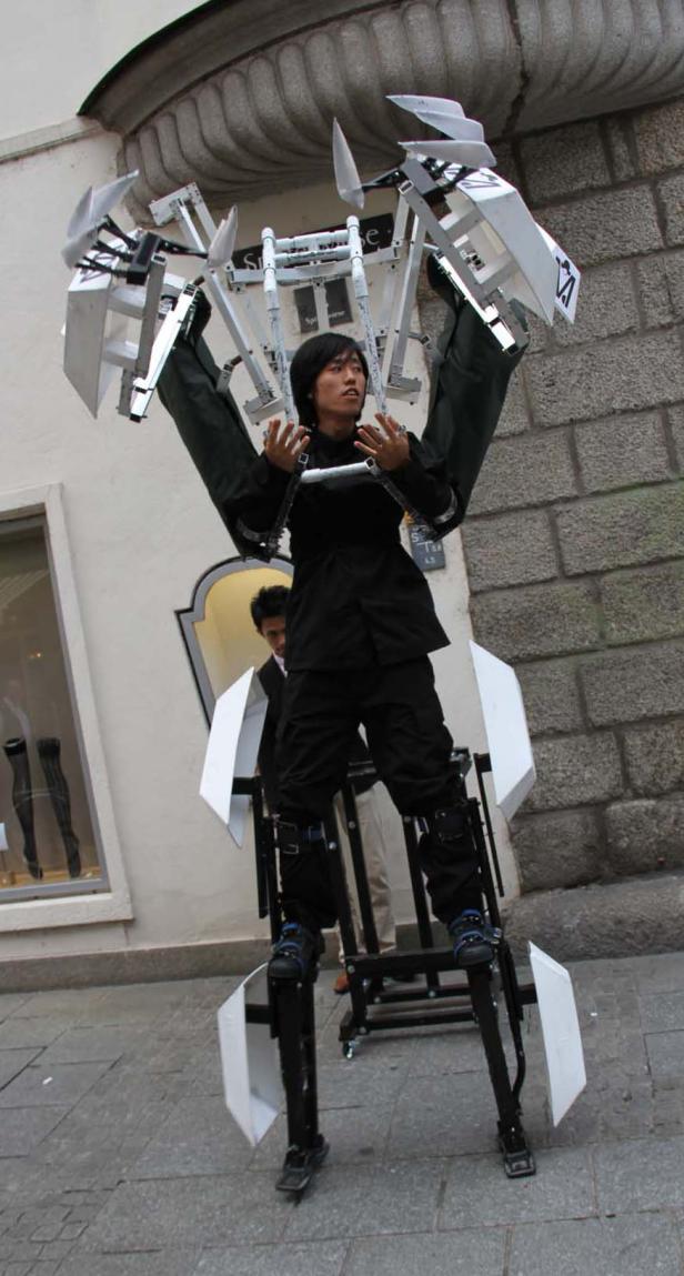 Ein Mann in einem schwarzen Anzug trägt eine große, skulpturale Apparatur.