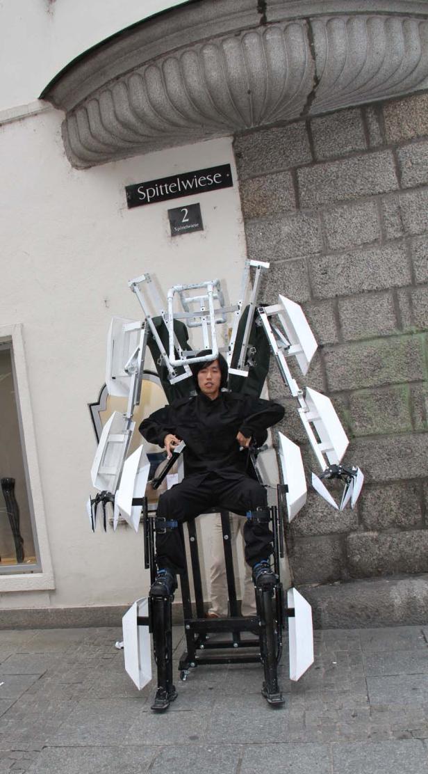 Ein Mann in einem Roboter-Exoskelett sitzt vor einem Gebäude in der Spittelwiese.