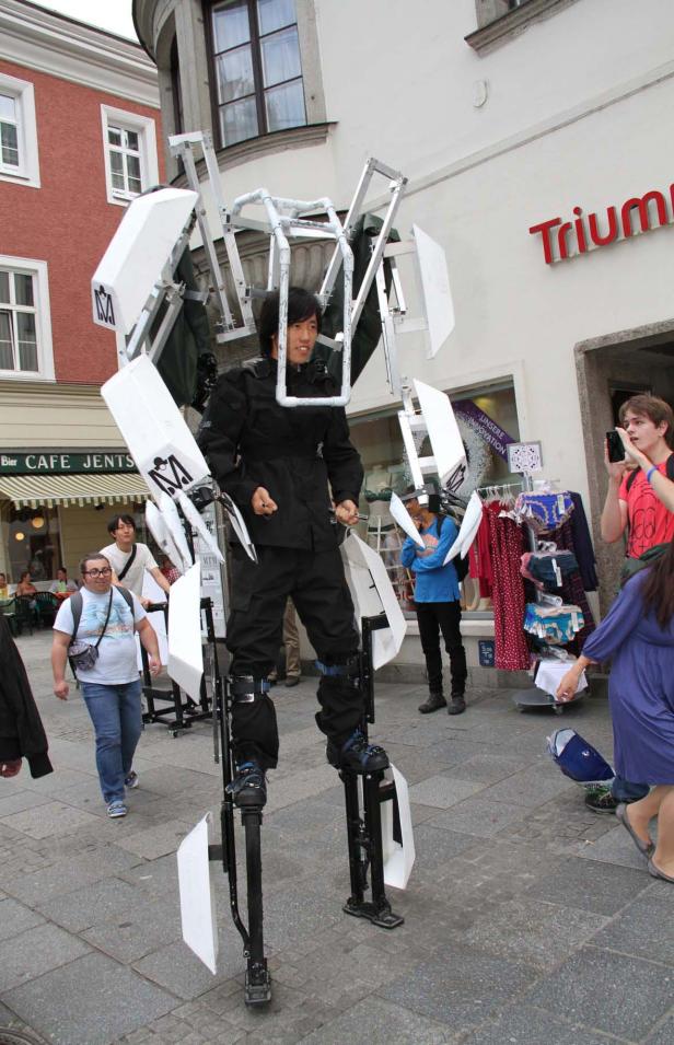 Ein Mann in einem Roboter-Kostüm auf Stelzen steht in einer belebten Straße.
