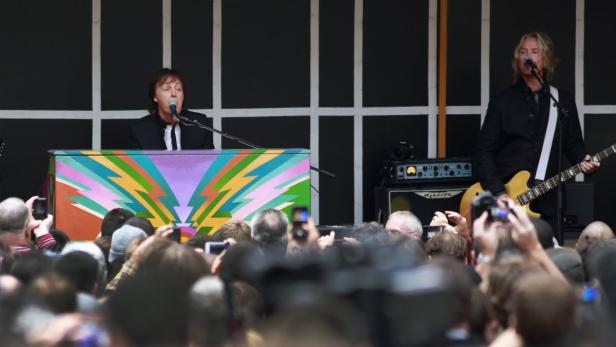 Paul McCartney spielt auf einem bunt bemalten Klavier, während ein Gitarrist daneben steht.