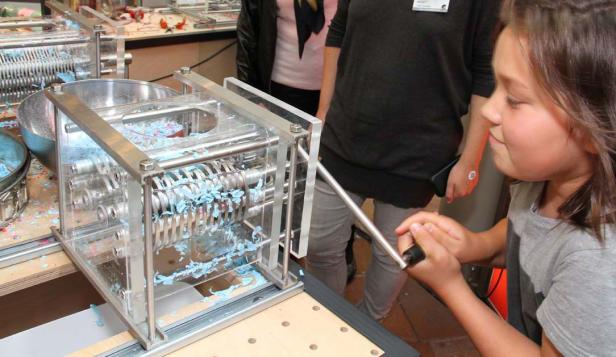 Ein Mädchen bedient eine Maschine, die blaue Seifenstücke zerkleinert.