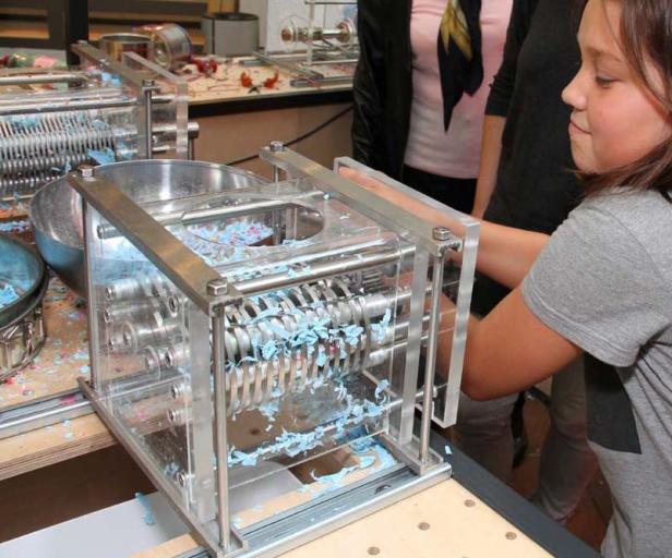 Ein Mädchen bedient eine Maschine, die blaue Seife in kleine Stücke schneidet.