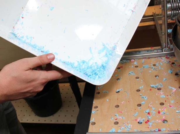 Eine Person leert eine Wanne mit blauen Papierresten über einem Tisch.