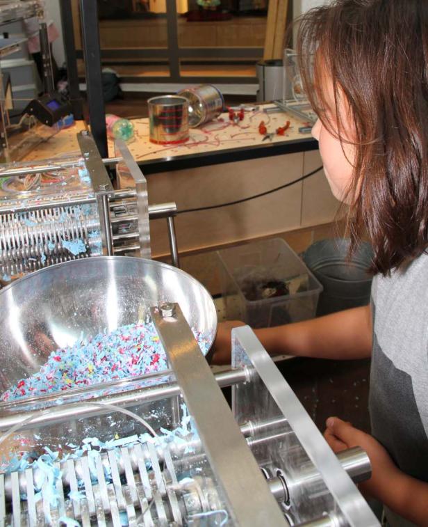 Ein Mädchen bedient eine Maschine, die bunte Wachsmalstifte zerkleinert.